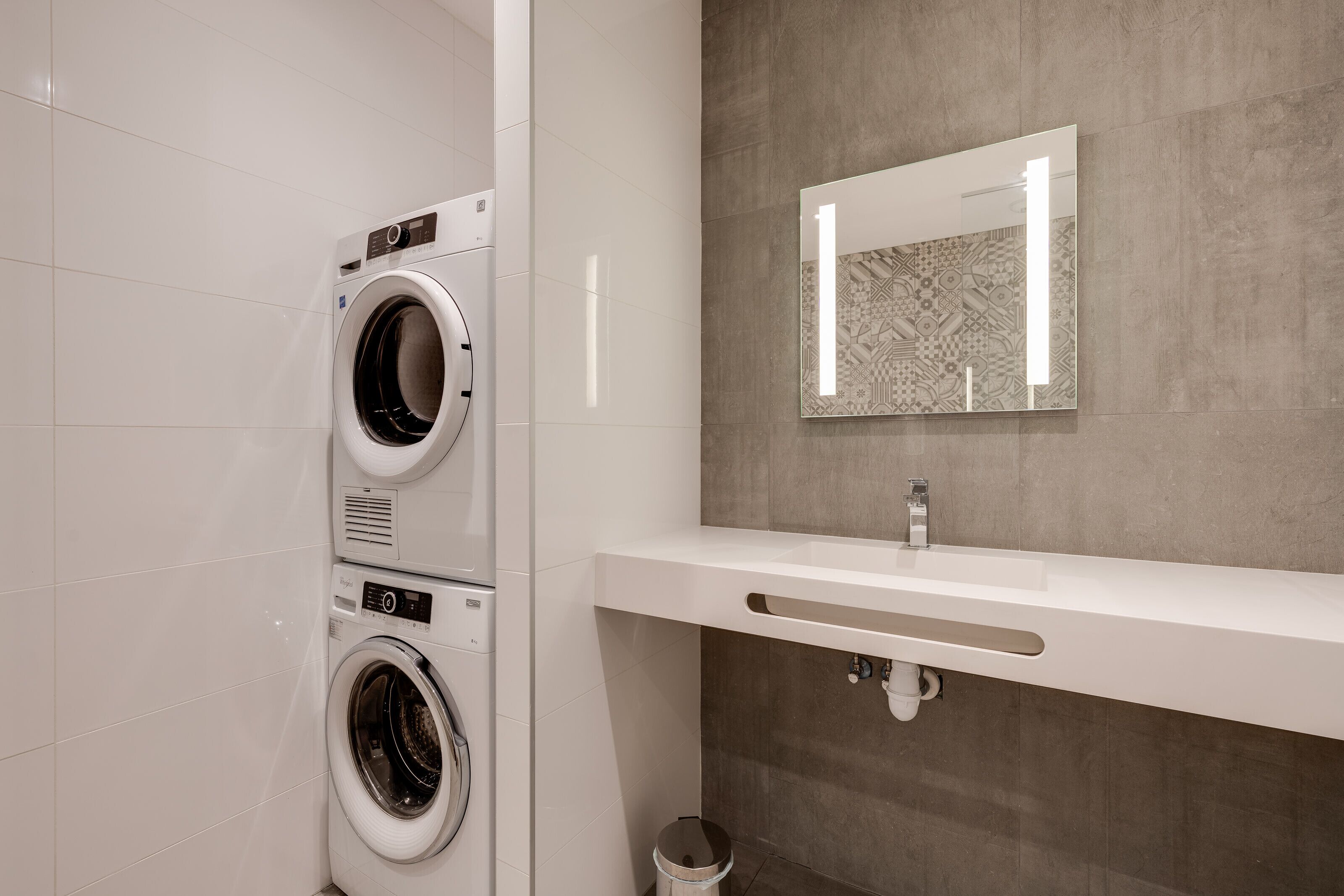 Une salle de bain moderne avec un lave-linge double, un grand miroir et un lavabo blanc.