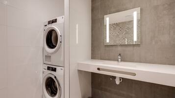 Une salle de bain moderne avec un lave-linge double, un grand miroir et un lavabo blanc.
