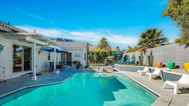 A swimming pool with lounge chairs and umbrellas, surrounded by a patio area with a mountain view. - Flora Vista Sunshine - A Ryson Property (Palm Springs)