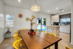 A modern kitchen with white cabinets, a wooden dining table, and yellow chairs.