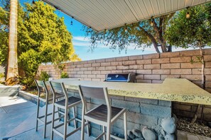 An outdoor patio with a brick wall, a table, and chairs. - Flora Vista Sunshine - A Ryson Property (Palm Springs)
