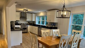 Una cocina moderna con armarios blancos, una isla central y un comedor con sillas y una mesa de madera.