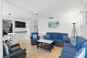 Ein großzügiger Wohnbereich mit blauem Sofa, Korbstühlen, einem Couchtisch und einem Deckenventilator.