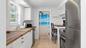 Una cocina con encimera de madera, armarios blancos, un refrigerador de acero inoxidable y vista a la playa a través de una puerta.