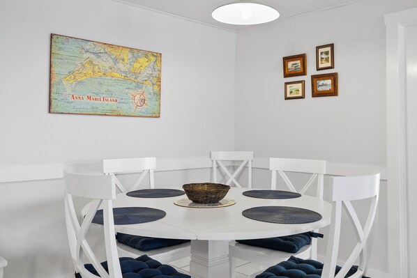 Un coin repas avec une table et des chaises blanches, une carte accrochée au mur et des tableaux encadrés.