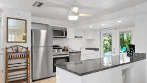 A modern kitchen with white cabinetry, stainless steel appliances, a wooden rack, and a view of a swimming pool. - Pool Party South · 3BR · Pool & Spa · Updated Jan 2025 (Holmes Beach)