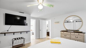 A bedroom with a bed, a TV mounted on the wall, a dresser, a mirror, and a ceiling fan. - Pool Party South · 3BR · Pool & Spa · Updated Jan 2025 (Holmes Beach)