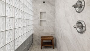 A bathroom with a tiled wall, a wooden bench, and a shower with a wall-mounted faucet. - Pool Party South · 3BR · Pool & Spa · Updated Jan 2025 (Holmes Beach)