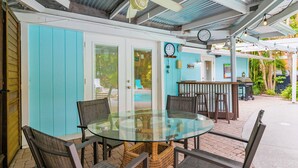A glass-top table with wicker chairs, a ceiling fan, and a clock on the wall. - Pool Party South · 3BR · Pool & Spa · Updated Jan 2025 (Holmes Beach)