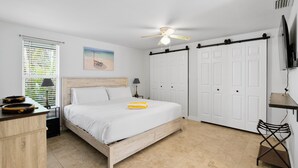 A bedroom with a bed, a ceiling fan, a desk with a lamp, a chair, and a TV on the wall. - Pool Party South · 3BR · Pool & Spa · Updated Jan 2025 (Holmes Beach)
