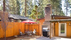 A backyard with a wooden fence, a barbecue grill, outdoor furniture, and a patio area.