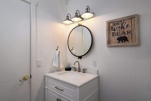 A bathroom with a white vanity, a round mirror, and a wall-mounted light fixture. - Pet Friendly Cabin Close to Beach & Slopes, Live Like a Local (Kings Beach)