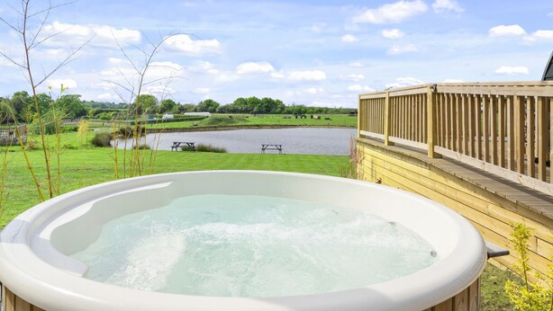 Un jacuzzi con vistas a un lago y una terraza de madera.