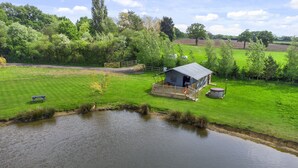 Una cabaña junto al lago con una terraza, un jacuzzi y un campo de césped.