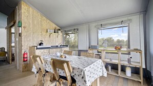 Cocina rústica con paredes de madera, una mesa de comedor cubierta con mantel blanco y vista a un jardín a través de una ventana.