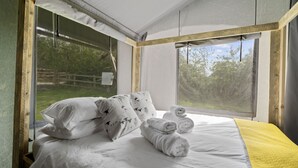 Un dormitorio con un ventanal grande, ropa de cama blanca y una manta amarilla.