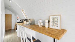 Una cucina moderna con un piano di lavoro in legno, mobili bianchi e un quadro con dei polli.