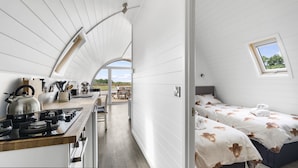 Una cucina compatta e moderna con piano cottura a gas e bollitore, una zona pranzo con tavolo e sedie in legno, e una camera da letto con un letto singolo e una finestra.