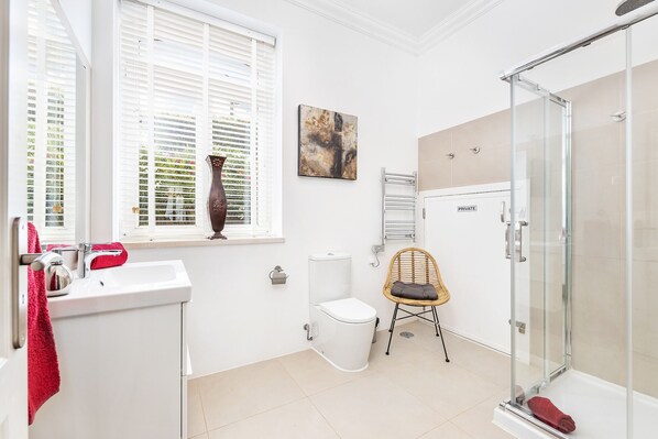 Un baño moderno con cabina de ducha de vidrio, un lavamanos blanco, inodoro y una silla de mimbre.