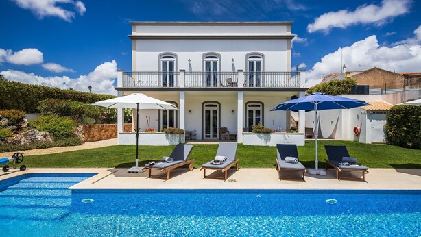 Una casa de dos pisos con piscina, camastros y sombrillas.