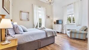 Un dormitorio con cama, mesita de noche, lámpara, cómoda, televisor y sofá.