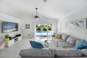 A modern living room with a grey sofa, a coffee table, a TV, and a ceiling fan. - 2041 Managed By Brampton Park (Pompano Beach)