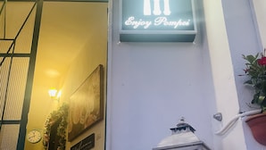 Entrada de hotel con un letrero que dice "B&B Enjoy Pompei", dos faroles blancos y un reloj en la pared.