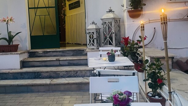 Entrada de un restaurante con terraza y plantas en macetas. Se lee un cartel: 'B & B Enjoy Pompei'.
