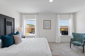 Um quarto com cama, duas janelas, uma cadeira e um abajur fixado na parede.