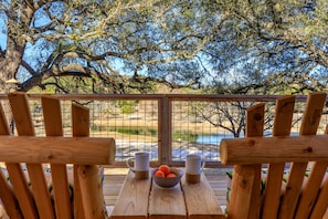 Una terraza de madera con una mesa, sillas, un cuenco de fruta y dos tazas.
