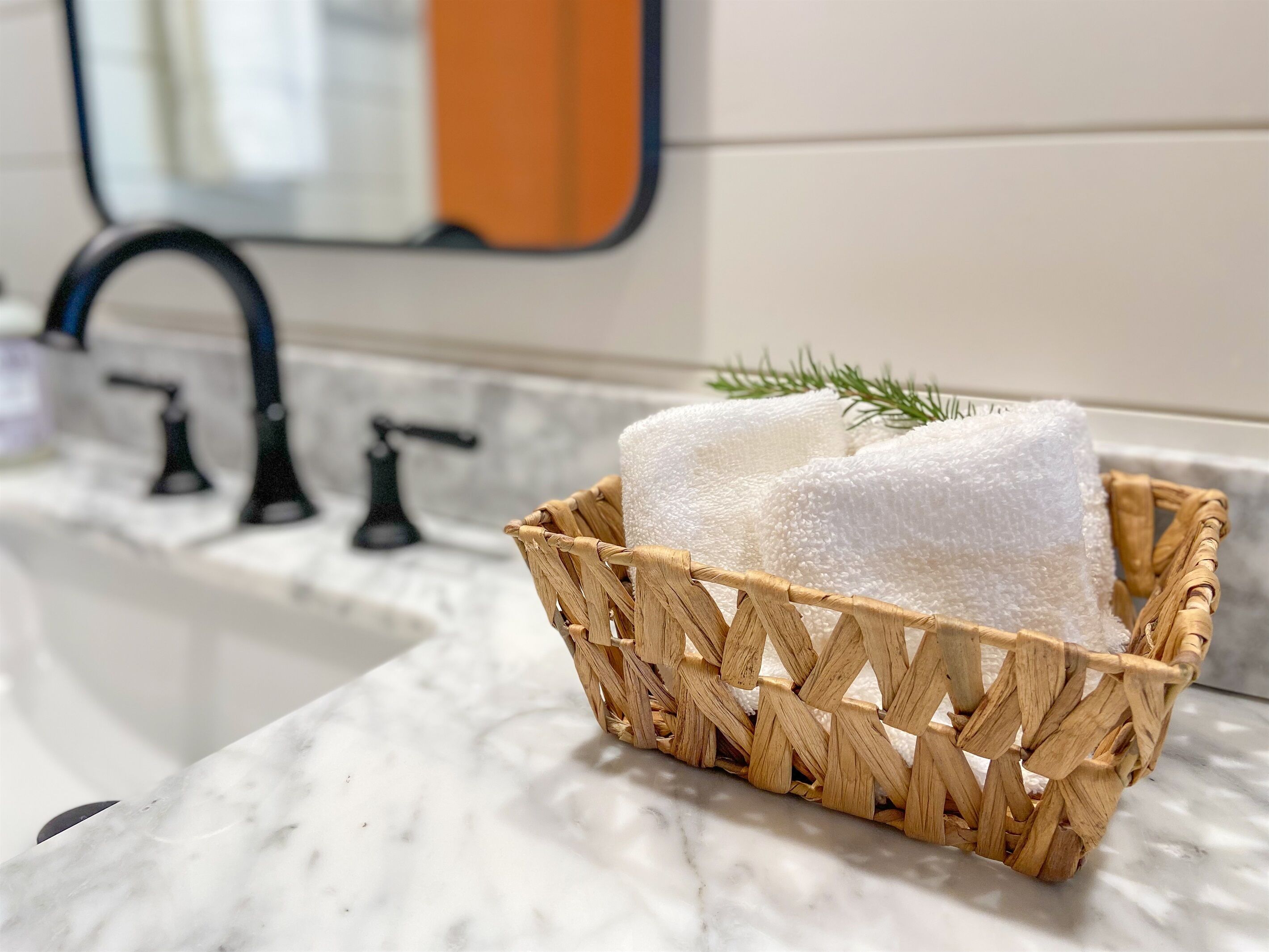 Une salle de bain avec un lavabo en marbre, un robinet noir et un panier tressé contenant une serviette blanche.