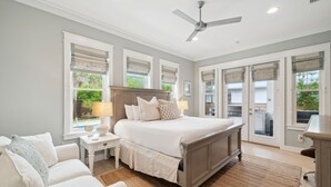 Une chambre avec un grand lit, un ventilateur de plafond et une vue sur le jardin à travers les fenêtres.
