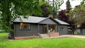A modern two-story house with a dark exterior, a front porch, and a well-maintained lawn. - Whimsical Midcentury Home with Game Room (Springfield)