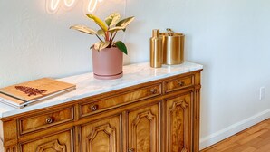 A wooden cabinet with drawers, a neon sign on the wall, a potted plant, and a few bottles on top. - Whimsical Midcentury Home with Game Room (Springfield)