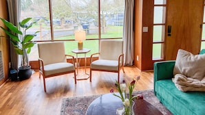 A room with two chairs, a small table with a lamp, a sofa, a potted plant, and a view of the outside. - Whimsical Midcentury Home with Game Room (Springfield)