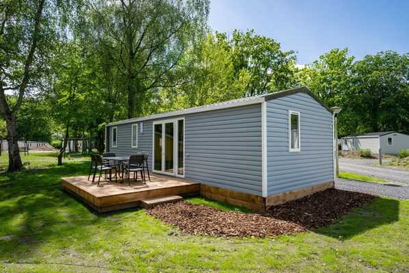 A small, single-story cabin with a patio area, a sliding glass door entrance, and a small deck. - EuroParcs Het Amsterdamse Bos (Amstelveen)
