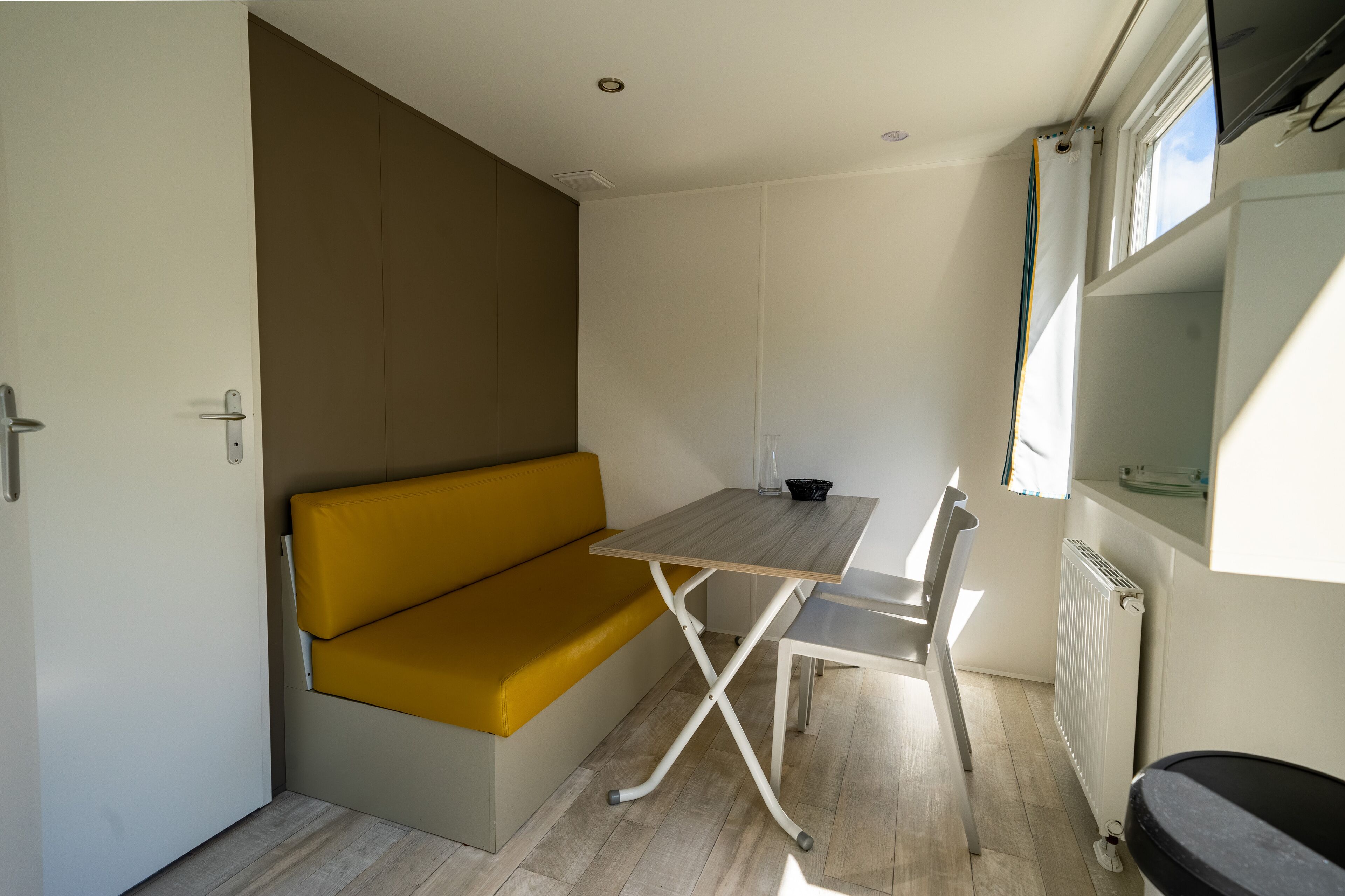 Una habitación pequeña con un sofá amarillo, una mesita, un radiador y una ventana.