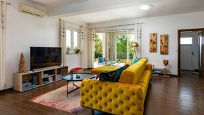Een moderne woonkamer met een geel sofa, een flatscreen televisie en een schuifdeur naar een balkon.