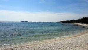 Een strand met helder water, een kiezelstrand en verre eilanden.