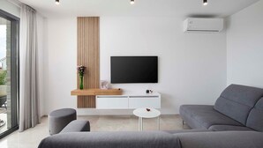 A modern living room with a grey sofa, a flat-screen TV mounted on a white console, and a wooden accent wall.