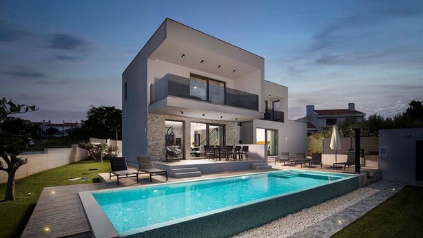 A modern two-story house with a swimming pool, outdoor seating, and a well-maintained lawn.