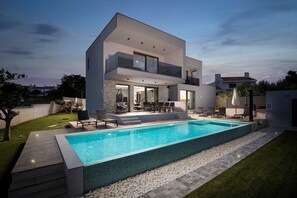 A modern two-story house with a swimming pool, outdoor seating, and a well-maintained lawn.