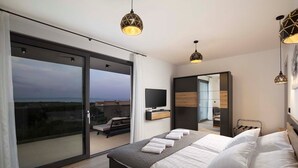 A modern bedroom with a large bed, a TV, and a balcony with a view.