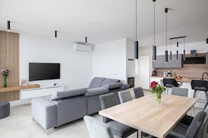 Una sala moderna con un sofá seccional gris, una mesa de comedor de madera y un televisor de pantalla plana montado en la pared.