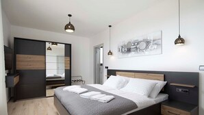A modern bedroom with a large bed, bedside tables, a wardrobe, and a mirror.
