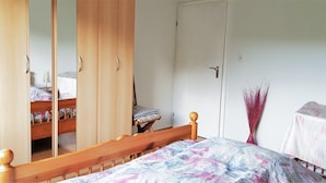 Een slaapkamer met een houten bed, een garderobe met spiegeldeuren, een nachtkastje en een kleine tafel met een vaas.