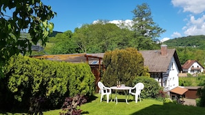 Een tuin met een tafel en stoelen, een houten pergola en een huis met een schuin dak.