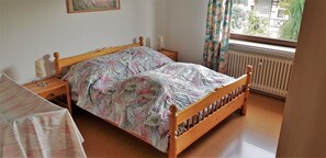 Un dormitorio con cama de madera, mesita de noche, radiador y ventana con cortinas.