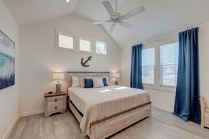 A bedroom with a bed, nightstands, a ceiling fan, a wall-mounted anchor decoration, and a window with blinds. - The best vacation memories are made at the beach! Golf cart available for rent, (Port Aransas)
