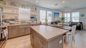 A modern kitchen with a central island, built-in appliances, and a dining area with a sofa and chairs. - The best vacation memories are made at the beach! Golf cart available for rent, (Port Aransas)